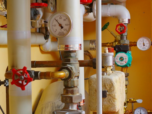 Sala técnica de aquecimento central com tubagens, válvulas e manómetros